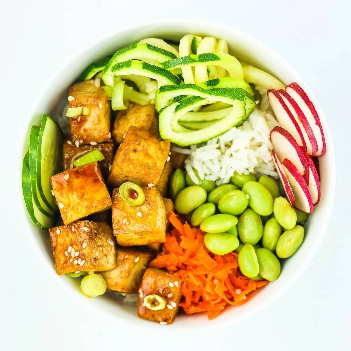 A bowl of Veggie Poke Bowl with non-GMO agedashi tofu, edamame, cucumber, seaweed salad, avocado, black sesame seeds, crispy onions, and Banzai signature poke sauce.